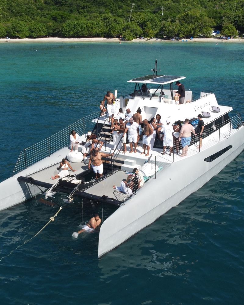 A group dressed in white aboard a catamaran anchored in turquoise water