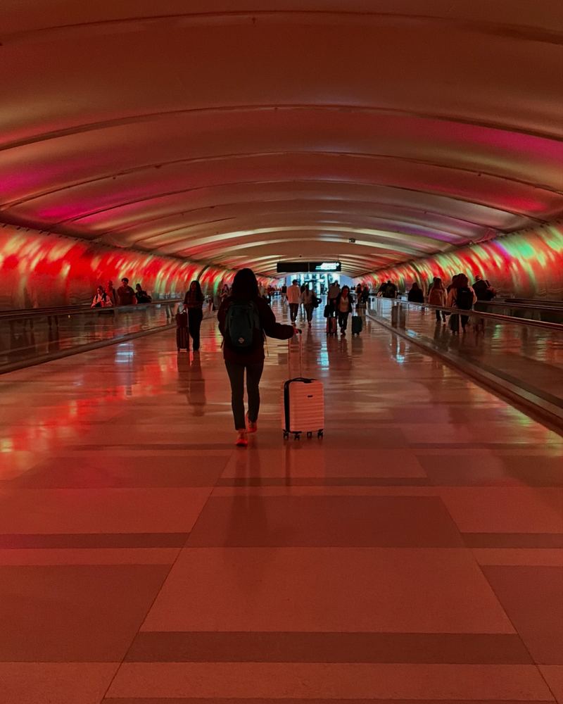 A lone traveler rolling a suitcase down a glowing airport tunnel